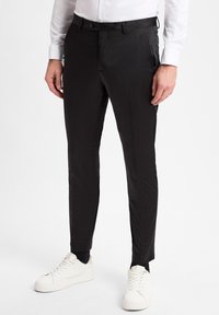 Schwarze Anzughosen mit schmaler Passform und geradem Schnitt. Aus glattem Stoff gefertigt, mit vorderen Taschen und einem Knopfverschluss. Kombiniert mit weißen Sneakers.
