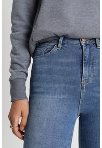 Přiléhavé tmavě modré džíny s jemnou texturou, doplněné šedým topem s dlouhým rukávem. Obsahuje standardní pas a přední kapsy.