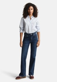 Blå- och vitrandig skjorta med knappar, kombinerad med mörkblå utsvängda jeans och bruna sneakers. Skjortan har uppvikta ärmar och en klassisk krage.