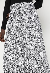 Gonna lunga e arricciata con un motivo floreale in bianco e nero. Presenta una vita elastica e una texture di tessuto fluido.