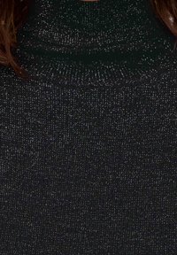 Gros plan sur un pull en tissu côtelé noir pailleté avec un col haut et des mèches de cheveux bruns sur les côtés.