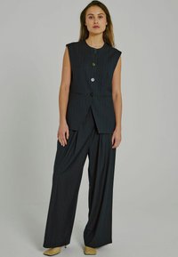 Gilet senza maniche a righe nere con chiusura a bottone, abbinato a pantaloni neri a taglio largo. Il tessuto presenta una texture liscia e un design su misura.