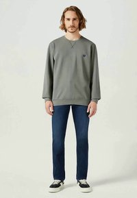 Sweatshirt cinzenta com mangas compridas, gola redonda e pequeno logótipo. Combinada com jeans azul escuro e ténis pretos com solas brancas.
