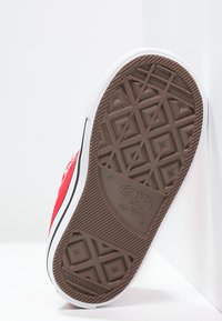 Rote Canvas-Sneaker mit weißer Gummisohle und Zehenkappe. Verfügt über eine braune Gummisohle mit Diamantmuster und einen schwarzen Streifen entlang der Kante.