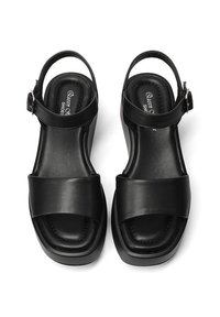 Sandali in pelle nera con una larga fascia anteriore, fascia regolabile alla caviglia e suola piattaforma moderata, caratterizzati da texture lisce e minimi dettagli.