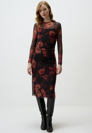 Long-sleeve, sheer mesh dress with a black base and red floral pattern. Fitted design with ruching at the waist, knee-length hem. Paired with black knee-high boots.