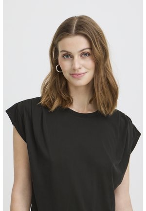 Young woman with shoulder-length light brown hair wearing silver hoop earrings and a black sleeveless top, smiling gently at the camera.