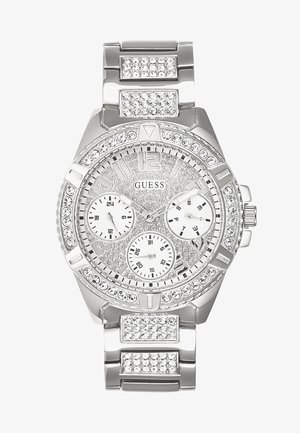 Hopeinen kello, jossa on kristallikoristeet, kolme alivalotinta, rohkeat tuntimerkit ja teksturoitu kellotaulu. Metallihihna lisää tyylikkään lopputuloksen.