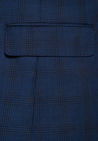 Granatowa tkanina w kratkę z czarnymi akcentami; zawiera kieszeń z prostym klapkiem.