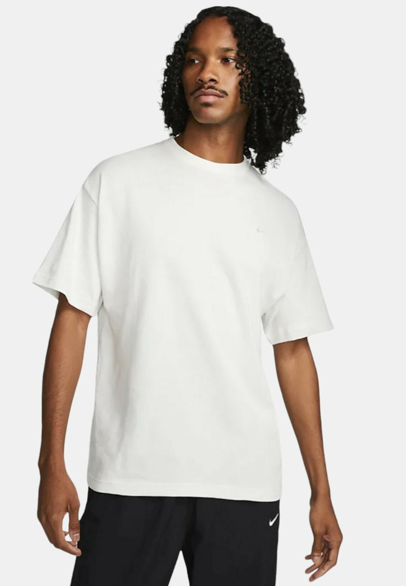 Vit bomull t-shirt med korta ärmar, rund halsringning och en liten blå logotyp på bröstet. Mjuk, avslappnad design, kombinerad med svarta byxor.