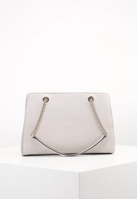 Sac à main beige au design structuré, avec une surface texturée, des poignées en chaîne argentées et des accents métalliques.