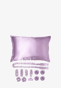 Oreiller en satin lavande avec des bords froncés, accompagné d'accessoires pour cheveux : élastiques à queue de cheval, chouchous et une pince à cheveux, tous dans des couleurs assorties.