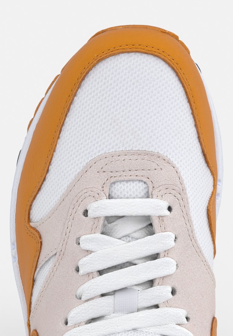Witte sneaker met oranje accenten, met een textuur bovenkant, zachte nubuck en platte witte veters op een afgeronde neusontwerp.