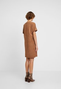 Braunes Wildlederkleid mit kurzen Ärmeln und geradem Schnitt, das oberhalb des Knies endet; kombiniert mit ankle boots im Schlangenmuster.