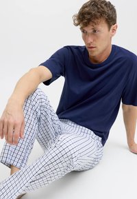 Tumši zils T-krekls ar apaļu kaklu, kopā ar baltiem pidžamas biksēm ar tumši zilu režģa rakstu. Mīksts audums, brīvs piegriezums, redzamas šuves detaļas.