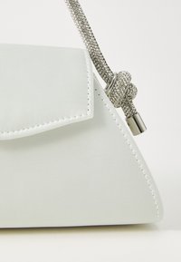 Borsa a tracolla bianca in satin con forma triangolare, dotata di chiusura a patta e tracolla in strass testurizzata. Presenti dettagli in metallo argentato.