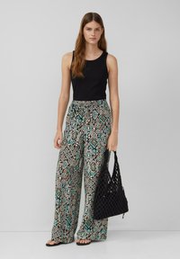 Top senza maniche nero, pantaloni larghi a fantasia nei toni del teal, nero e crema, e una borsa a tracolla intrecciata nera. Sandali piatti neri.