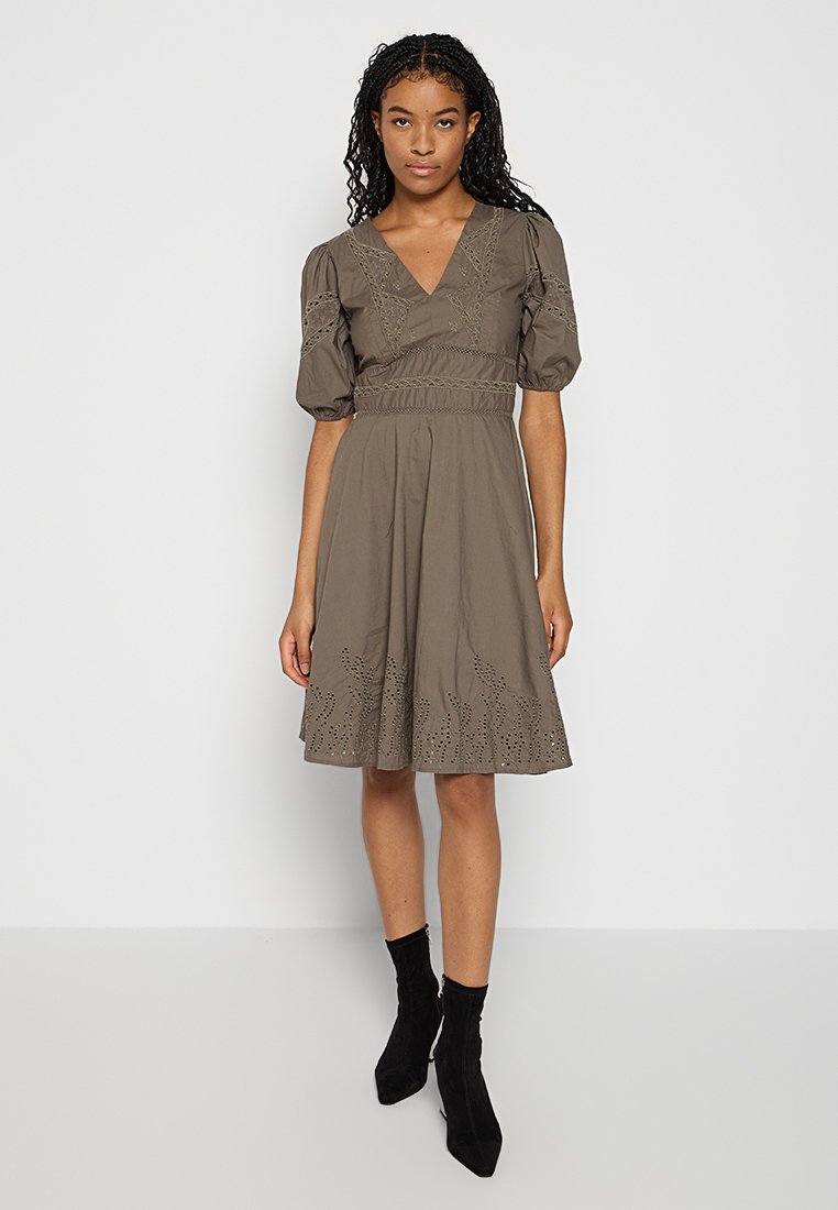 Braunes Baumwollkleid mit Puffärmeln, einem V-Ausschnitt und bestickten Details am Saum. Tragen mit schwarzen Knöchelstiefeln.