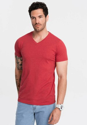Rotes V-Ausschnitt-T-Shirt aus weichem Stoff, kurze Ärmel, schmaler Schnitt. Das Modell trägt hellblaue Jeans und eine große weiße Uhr.