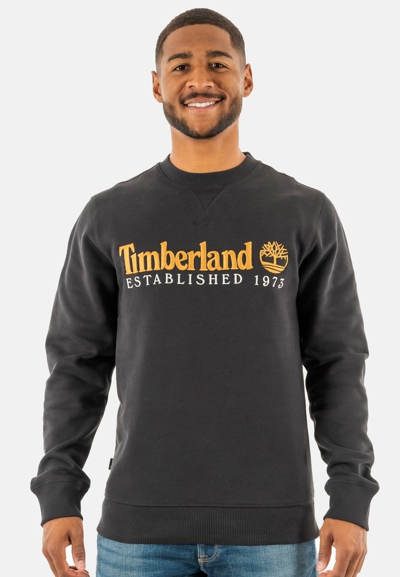 Zwarte sweatshirt van zacht materiaal met "Timberland Established 1973" in gouden borduursel en een boomlogo. Geribde mouwen en onderrand.