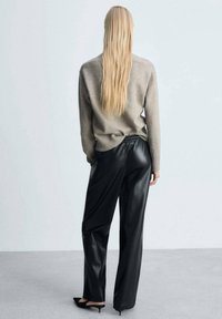 Pull en laine gris clair associé à un pantalon en cuir noir taille haute. Le pantalon a une coupe ample et une ceinture élastique. Ballerines noires à bouts pointus.