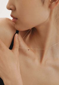 Collar plateado delicado con un pequeño colgante que presenta acentos rojos, llevado sobre piel desnuda, destacando su cadena y diseño minimalista.