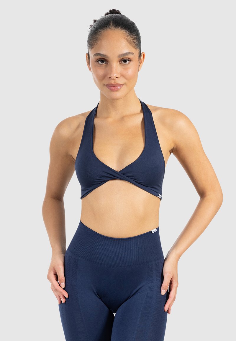 Marinblå sport-bh med djup V-ringning och överlappande design, tillverkad av elastiskt material; i kombination med högmidjade matchande leggings.