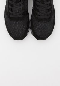 Chaussures de sport en mesh noir avec lacets, vues de dessus sur un fond blanc, montrant la texture détaillée et les coutures.