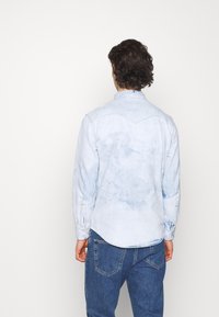 Camicia in denim azzurro chiaro con maniche lunghe, colletto a punta e orlo curvo, caratterizzata da una texture scolorita e polsini con bottoni.