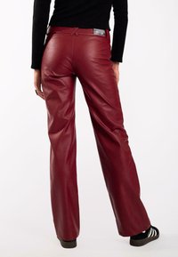 Pantalones de cuero carmesí con una textura suave, diseño de pierna ancha y cintura alta. Presenta una etiqueta en la parte posterior cerca de la cintura.
