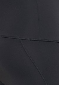 Leggings de sport noirs avec une texture lisse et extensible. Comptent des coutures surpiquées et des panneaux pour un ajustement structuré.