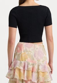 Černý žebrovaný crop top s krátkými rukávy, s širokým výstřihem a upnutým střihem, v kombinaci s vrstvenou sukní s květinovým vzorem.