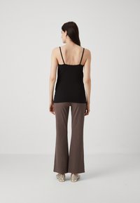 Black sleeveless top paired with brown flared pants, featuring a subtle textured pattern, and metallic-accented shoes.