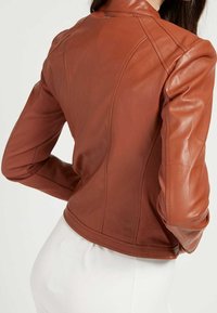 Blouson en cuir marron avec un design ajusté, texture lisse et coutures structurées. Le blouson a une longueur courte et un petit col.
