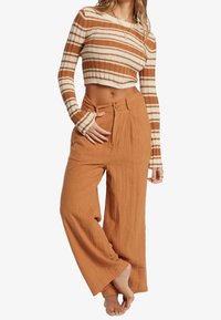 Pasiasty top crop w kolorze pomarańczowym i kremowym, połączony z szerokimi, teksturowanymi spodniami w kolorze rdzy, z wiązaniem w pasie i dwoma przednimi guzikami.