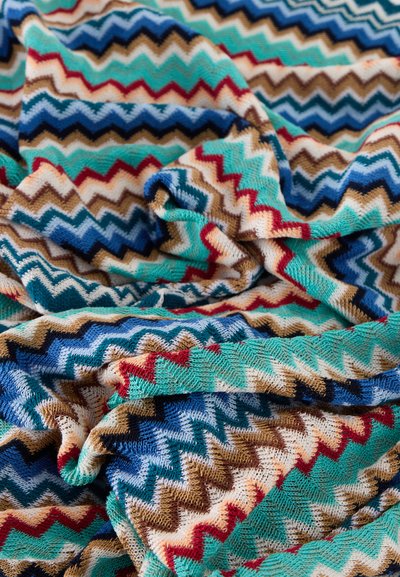 Απαλό πλεκτό ύφασμα με πολύχρωμο ζιγκ-ζαγκ μοτίβο σε μπλε, τιρκουάζ, κόκκινο, καφέ και λευκό, εμφανιζόμενο με πτυχώσεις και λεπτομέρειες υφής.