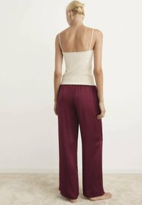 Top beige con spalline sottili abbinato a pantaloni ampi bordeaux. L'outfit presenta una texture liscia e una vestibilità rilassata, adatto per un abbigliamento informale.
