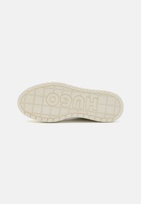 Suola di sneakers in gomma, colore crema, superficie testurizzata con motivi quadrati, presenta "HUGO" in evidenza con caratteri in grassetto.