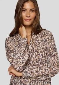 Langärmlige Bluse aus leichtem Stoff mit Leopardenmuster in Braun, Beige und Creme, mit gerafften Bündchen und einem Ausschnitt mit Schlitz.