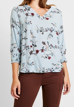 Blusa de cuello en V floral en azul claro, con flores blancas y burdeos, mangas 3/4 con puños elásticos y un corte holgado.