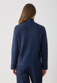 Pulover navy din lână moale, cu guler înalt, textură ribbed pe mâneci și o croială lejeră cu tiv drept.