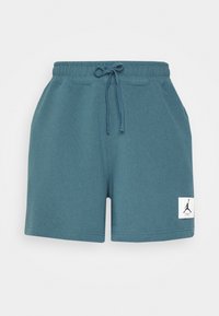 Shorts à taille élastique bleu sarcelle avec cordon, poches latérales et une petite étiquette blanche avec un logo en silhouette noire sur la jambe gauche.