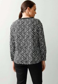 Zwart-wit lange mouw top met een draaiend patroon, een gladde textuur en een relaxte pasvorm, gecombineerd met zwarte broek.