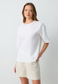 Witte linnen t-shirt met een ronde halslijn, korte mouwen en een relaxte pasvorm, gecombineerd met lichtbeige linnen shorts.