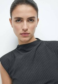 Haut sans manches à rayures noires et blanches avec un col montant. Tissu doux à légère brillance, avec des détails ajustés et un drapé subtil.