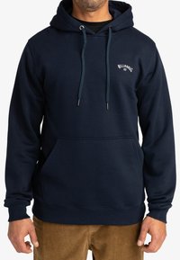 Sudadera azul marino con un bolsillo frontal, cordones ajustables y un pequeño logo en el pecho. Fabricada con un material suave y texturizado.
