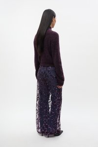 Fialový chlupatý svetr nošený s průhlednou tmavě modrou sukní zdobenou fialovými flitry, vytvářející texturovaný a vrstvený vzhled.