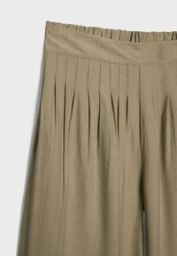 Jupe plissée marron clair taille haute avec une ceinture élastique et un tissu texturé, présentée sur un fond uni.