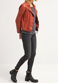 Czerwona skórzana kurtka motocyklowa z zamkami, szary sweter i czarne obcisłe dżinsy. Czarne botki za kostkę z elastycznymi bokami i teksturowaną podeszwą.