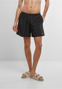 Sorte svøm shorts med elastisk talje, sidelommer og et lille gult logo. Letvægts, glat tekstur med en afslappet pasform.